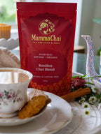 Mamma Chai Rooibos Chai Blend package on a table with a cup of tea and cookies.